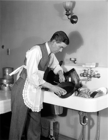 1930s MAN DRESSED IN SHIRT TIE VEST & APRON BENT OVER A SINK FULL OF DISHES CLEANING AN IRON SKILLET WITH A DISHCLOTH Stock Photo - Rights-Managed, Code: 846-02793180