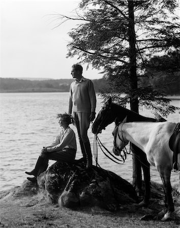 simsearch:846-02792220,k - 1930s MAN STANDING ON ROCK LAKESIDE HOLDING REINS OF TWO HORSES WITH WOMAN SEATED BESIDE HIM LOOKING OFF TO SIDE Stock Photo - Rights-Managed, Code: 846-02793190