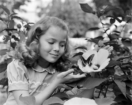 1950s PRETTY LITTLE GIRL SMILING AT HIBISCUS FLOWER & BUTTERFLY IN GARDEN Stock Photo - Rights-Managed, Code: 846-02793625