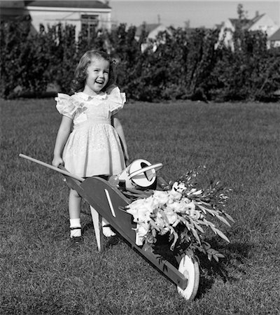 1950s SMILING GIRL WALKING YARD PUSHING CHILDS WHEELBARROW WITH FLOWERS WATERING CAN GARDENING Stock Photo - Rights-Managed, Code: 846-02793650