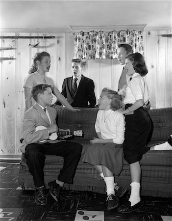 1950s GROUP SIX TEENAGERS THREE BOYS THREE GIRLS SITTING ON COUCH DEN REC ROOM BOY PLAYING UKULELE OTHERS SINGING SONG MUSIC Foto de stock - Con derechos protegidos, Código: 846-02793708