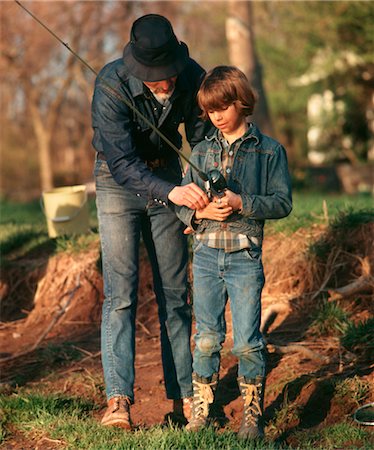 retro fishing - 1970s BOTH WEARING DENIM CLOTHING MAN FATHER TEACHING BOY SON HOW TO USE FISHING POLE AND REEL Stock Photo - Rights-Managed, Code: 846-02793889