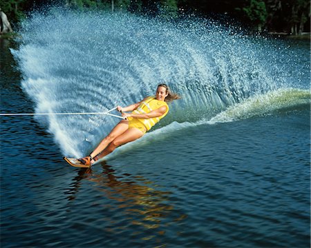 1970s YOUNG WOMAN WATER SKIING THROWING UP WATER FAN SPLASH WEARING LIFE JACKET YELLOW SWIMSUIT SPORTS Stock Photo - Rights-Managed, Code: 846-02793899