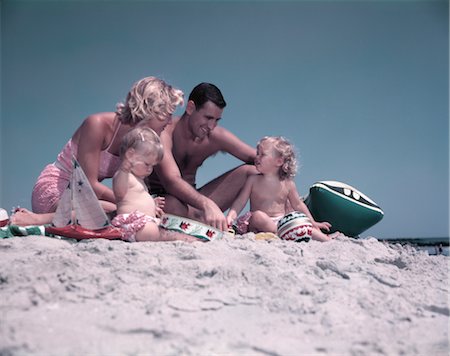 1950s FAMILY SITTING ON SANDY BEACH MAN WOMAN MOTHER FATHER TWO CHILDREN BOY GIRL PLAYING SAND TOYS SUMMER VACATION Foto de stock - Con derechos protegidos, Código: 846-02793937