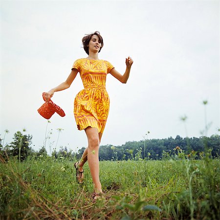 energetic fashion female - 1970s YOUNG WOMAN WEARING COLORFUL PRINT DRESS RUNNING IN FIELD CARRYING RED STRAW HAT Stock Photo - Rights-Managed, Code: 846-03164536