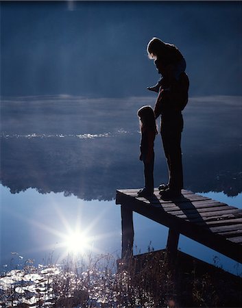 MOODY SILHOUETTE OF MAN FATHER AND TWO DAUGHTERS ONE ON HIS SHOULDERS OTHER STANDING ON DOCK LOOKING AT LAKE Stock Photo - Rights-Managed, Code: 846-03164862