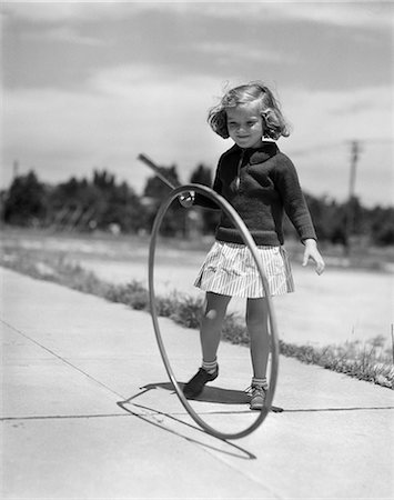 ANNÉES 1930 FILLE JOUANT AVEC CERCEAU ET BÂTON SUR TROTTOIR Photographie de stock - Rights-Managed, Code: 846-03163564