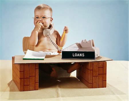 release - 1960s BABY BUSINESSMAN DIAPER SITTING AT TOY DESK LOANS BANK SIGN WEARING EYEGLASSES TALKING ON TELEPHONE Stock Photo - Rights-Managed, Code: 846-03163979