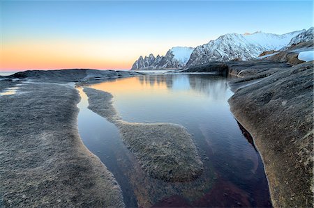 sunset mountains - Orange sky at sunset reflected on snowy peaks and the frozen sea surrounded by rocks Tungeneset, Senja, Troms County, Arctic, Norway, Scandinavia, Europe Stock Photo - Rights-Managed, Code: 841-08821538