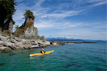 A water level view of a sea kayaker paddling in calm waters along a shoreline near Juneau, Inside Passage, Southeast Alaska, Summer Stock Photo - Rights-Managed, Code: 854-05974235