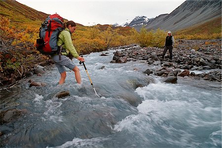 snow mountain trees river - Female backpacker makes her way across a cold rushing creek while her male companion watchs from the far shore. During Fall at Wrangell-St.Elias National Park in Southcentral Alaska. Stock Photo - Rights-Managed, Code: 854-02955227