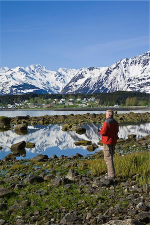 Man standing near shoreline viewing the community of Haines in the distant. Summer in Southeast Alaska. Stock Photo - Rights-Managed, Code: 854-02955590