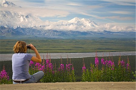 simsearch:854-03538162,k - Young woman sits on the ground looking through binoculars viewing Mt McKinley and the Alaska Range Denali National Park Alaska Stock Photo - Rights-Managed, Code: 854-03538132