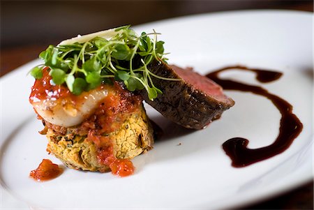 Kobe Beef Tenderloin Roasted and sliced and accompanied by bronzed Alaskan weathervane scallop and served over a Yukon Gold potato cake with fresh baby arugula, shaved Asiago cheese, balsamic veal reduction and roasted tomato preserves Stock Photo - Rights-Managed, Code: 854-03538362