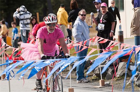 Senior man dressed in a pink shirt and tutu costume bikes across the finish line during the Pink Cheeks Triathlon, Seward, Southcentral Alaska, Summer Stock Photo - Rights-Managed, Code: 854-03846009