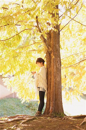poncho - Japanese woman in a white cardigan with a Smartphone leaning against a tree Stock Photo - Rights-Managed, Code: 859-06404986
