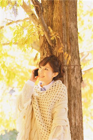 poncho - Japanese woman in a white cardigan on the phone leaning against a tree Stock Photo - Rights-Managed, Code: 859-06404988