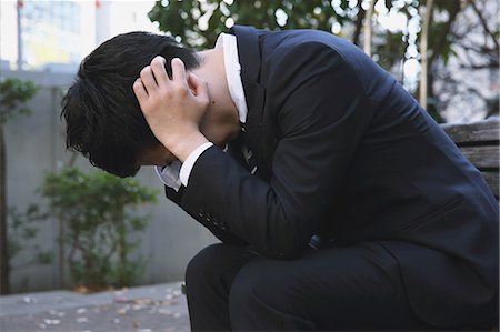 Desperate Japanese young businessman in a suit sitting on a bench in a park Stock Photo - Rights-Managed, Code: 859-07711099