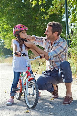 family on path - Father closing the helmet of her daughter on a bike Stock Photo - Rights-Managed, Code: 853-05840929