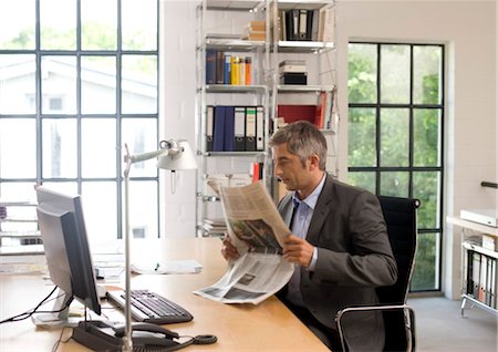 Businessman reading a newspaper at his desk Stock Photo - Rights-Managed, Code: 853-03459129