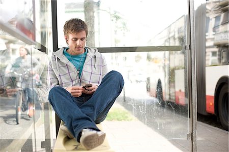 Young man sitting in a bus stop and using a mp3-player, low angle view Stock Photo - Rights-Managed, Code: 853-03459122