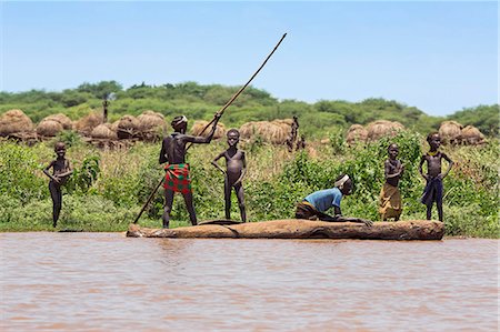 ethiopia - A man poles a dugout canoe past a Dassanech village near the banks of the Omo River, Ethiopia Stock Photo - Rights-Managed, Code: 862-06676695