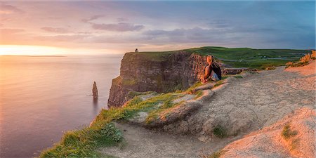 Cliffs of Moher (Aillte an Mhothair), Doolin, County Clare, Munster province, Ireland, Europe. Panoramic view with a woman watching the sun setting from the top of the cliff. Stock Photo - Rights-Managed, Code: 862-08699403