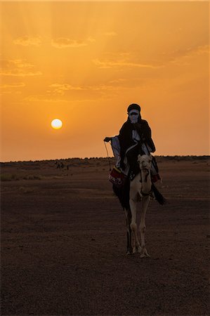 simsearch:862-03437232,k - Niger, Agadez, Dabous. A Tuareg man rides his camel across the desert at sunset. Stock Photo - Rights-Managed, Code: 862-08704972