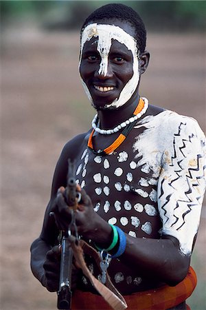 simsearch:862-03820434,k - Un guerrier Nyangatom a peint son corps et le visage en préparation pour une danse. Mâles plus adultes portent des fusils comme symboles de statut et dans le cas de raids des bovins ou des différends avec les tribus voisines. Le Nyangatom ou Bume sont une tribu nilotique de pasteurs semi-nomades qui vivent le long des rives du fleuve Omo dans le sud-ouest de l'Éthiopie. Photographie de stock - Rights-Managed, Code: 862-03354063