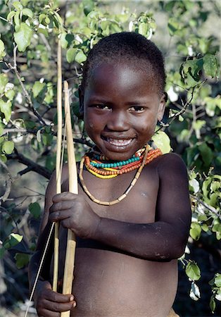 simsearch:862-03820241,k - A Hadza boy carrying a bow and arrow. The Hadzabe are a thousand-strong community of hunter-gatherers who have lived in the Lake Eyasi basin for centuries. They are one of only four or five societies in the world that still earn a living primarily from wild resources. Stock Photo - Rights-Managed, Code: 862-03355168