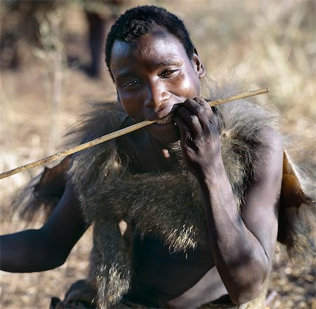 simsearch:862-03821015,k - A Hadza hunter wearing a baboon skin cape straightens a new arrow shaft in his teeth.The Hadzabe are a thousand-strong community of hunter-gatherers who have lived in the Lake Eyasi basin for centuries. They are one of only four or five societies in the world that still earn a living primarily from wild resources. Foto de stock - Con derechos protegidos, Código: 862-03355172