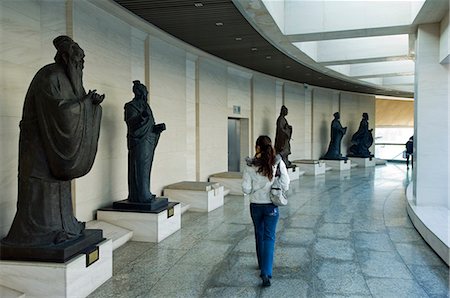 sculpture gallery - China,Beijing,The China Millenium Monument Museum. A girl is walking past figures of historical significance including Confucius. . Stock Photo - Rights-Managed, Code: 862-03351433