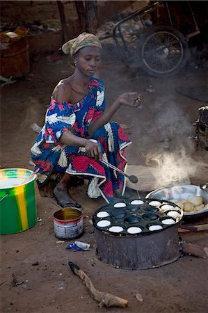 Mali,Bamako,Tinan. A Woman cooks muffins on a wood stove beside the road at the busy weekly market of Tinan situated between Bamako and Segou. Stock Photo - Rights-Managed, Code: 862-03364125