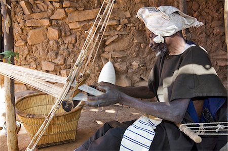 Mali,Dogon Country. An old man operates a narrow loom at Songho,an attractive Dogon village on top of the Bandiagara escarpment. Mali is Africa’s second largest producer of cotton. Stock Photo - Rights-Managed, Code: 862-03364179