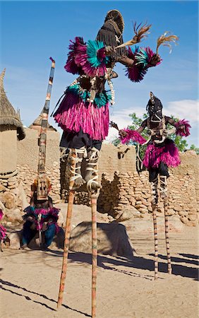 simsearch:400-06076338,k - Mali,Dogon Country,Tereli. Masked stilt dancers wearing coconut shells as breasts perform at the Dogon village of Tereli. Tereli is situated among rocks at the base of the spectacular 120-mile-long Bandiagara escarpment. The mask dance is staged at funeral ceremonies to appease the dead and speed them on their way to the ancestral world. Stock Photo - Rights-Managed, Code: 862-03364206