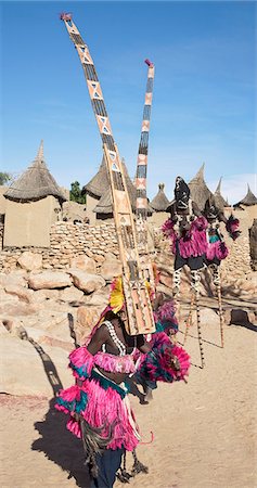 simsearch:400-05910051,k - Mali,Dogon Country,Tereli. Masked dancers wearing the fifteen-foot-high Sirige mask and stilt dancers perform at the Dogon village of Tereli which is situated among rocks at the base of the spectacular 120-mile-long Bandiagara escarpment. The mask dance is staged at funeral ceremonies to appease the dead and speed them on their way to the ancestral world. Stock Photo - Rights-Managed, Code: 862-03364202
