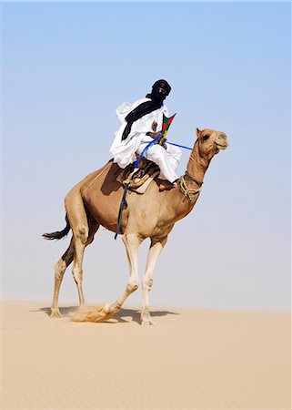 Mali,Timbuktu. In the desert north of Timbuktu,a Tuareg man rides his camel across a sand dune. He steers the animal with his feet. Stock Photo - Rights-Managed, Code: 862-03364258