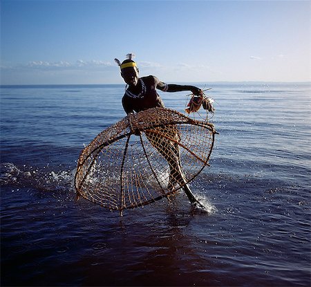 simsearch:862-03366124,k - With his traditional fishing basket poised,a Turkana fisherman rushes to catch a tilapia in the shallow waters of Lake Turkana. The conical shaped basket,three to four feet wide at the mouth and made from pliable sticks and twisted doum palm fronds,has a small flap at the top of the cone through which trapped fish are removed. Stock Photo - Rights-Managed, Code: 862-03366080