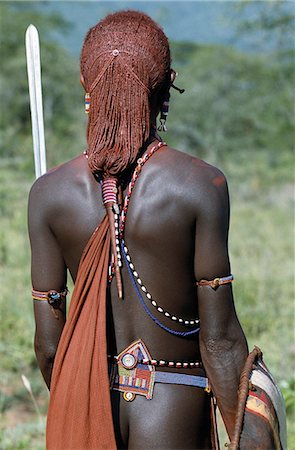 A back view of a Maasai warrior resplendent with long ochred braids tied in a pigtail. This singular hairstyle sets him apart from other members of his society. His beaded belt is of a style only worn by warriors. The little copper bell-shaped ear ornament hanging from his elongated and decorated earlobe is also peculiar to the Maasai. Foto de stock - Con derechos protegidos, Código: 862-03366153