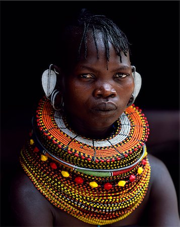 A Turkana woman sitting in the doorway of her hut. Her heavy mporro braided necklace identifies her as a married woman. Typical of her tribe,she wears many layers of bead necklaces and a beaded headband. Stock Photo - Rights-Managed, Code: 862-03366497