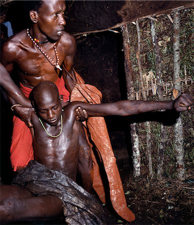 simsearch:862-03366174,k - A Samburu youth is carried by his sponsors into his mother's house to rest just after he has been circumcised in the early morning. Boys are not allowed to show any sign of fear or pain. Even the blink of an eyelid is frowned upon. It takes a good circumciser a minute to finish the operation and move quickly on to his next customer. Stock Photo - Rights-Managed, Code: 862-03366548