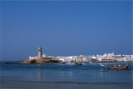 sur - A fishing dhow motors across the lagoon towards the sea in front of the lighthouse and whitewashed houses of the village of Al Ayja behind Stock Photo - Rights-Managed, Code: 862-03360195