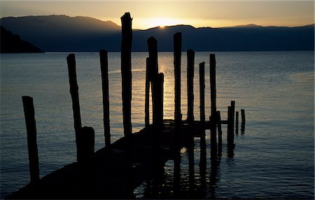 simsearch:862-07495921,k - The sun sets behind the hills across Lake Atitlan creating a silhouette of an old fishing jetty Stock Photo - Rights-Managed, Code: 862-03711714