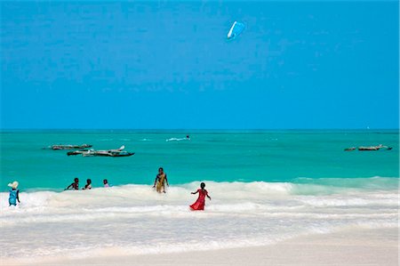 family beach kites - Tanzania, Zanzibar. Children play in the shallows off Paje Beach while a kite surfer displays his skill in the turquoise sea. Stock Photo - Rights-Managed, Code: 862-03737281