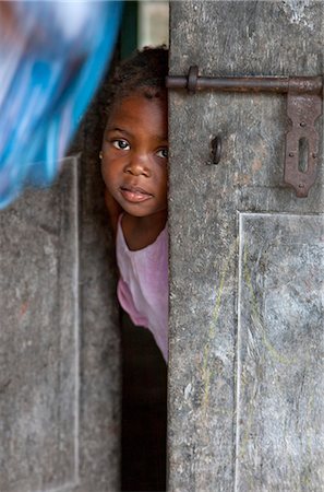 shy baby - Tanzanie, Zanzibar. Une jeune fille peeps en dehors de la porte d'entrée de sa maison à Nungwi, la pointe nord de l'île de Zanzibar. Photographie de stock - Rights-Managed, Code: 862-03737294