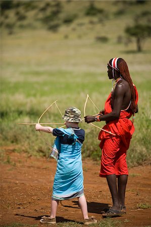 Kenya, Laikipia, Lewa Downs.  One of the Maasai guides teaches archery to a child on safari. Stock Photo - Rights-Managed, Code: 862-03731620