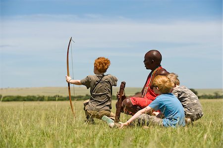 Kenya, Masai Mara.  Safari guide, Salaash Ole Morompi, teaches children archery Maasai style. Stock Photo - Rights-Managed, Code: 862-03731741