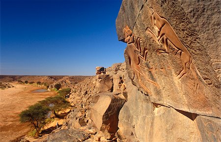 Libya, Fezzan, Messak Settafet. A petroglyph of felines, known as the 'dancing cats' -stands by a ledge high above Wadi Mathendusch. Stock Photo - Rights-Managed, Code: 862-03731771