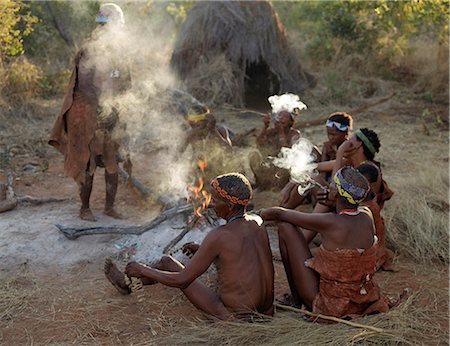 simsearch:862-03820241,k - A group of NIIS hunter gatherers sit round their fire and smoke.They are a part of the San people, often referred to as Bushmen.They differ in appearance from the rest of black Africa having yellowish skin and being lightly boned, lean and muscular.They live in the harsh environment of a vast expanse of flat sand and bush scrub country straddling the Namibia Botswana border. Stock Photo - Rights-Managed, Code: 862-03820229