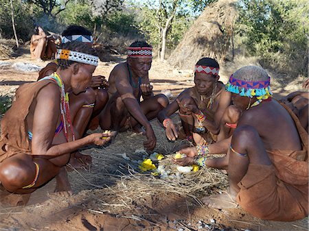 simsearch:862-03821015,k - A group of NIIS hunter gatherers enjoy eating an ostrich egg, which has been baked in the embers of a fire.The NIIS are a part of the San people, often referred to as Bushmen.They differ in appearance from the rest of black Africa having yellowish skin and being lightly boned, lean and muscular. Foto de stock - Con derechos protegidos, Código: 862-03820235